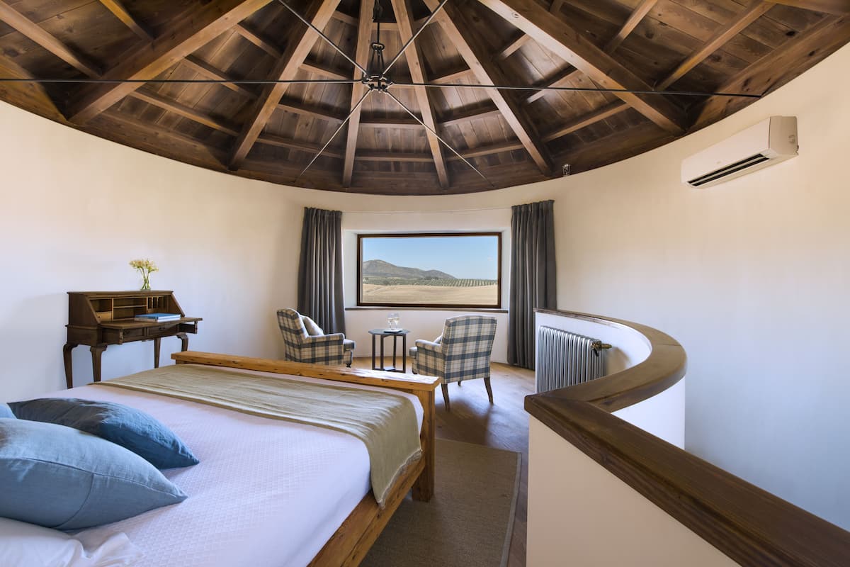 A bedroom with a large bed, a desk, two chairs, a view of the desert, and a curved balcony.