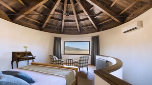 Un dormitorio con una cama grande, un escritorio, dos sillas, vistas al desierto y un balcón curvo.