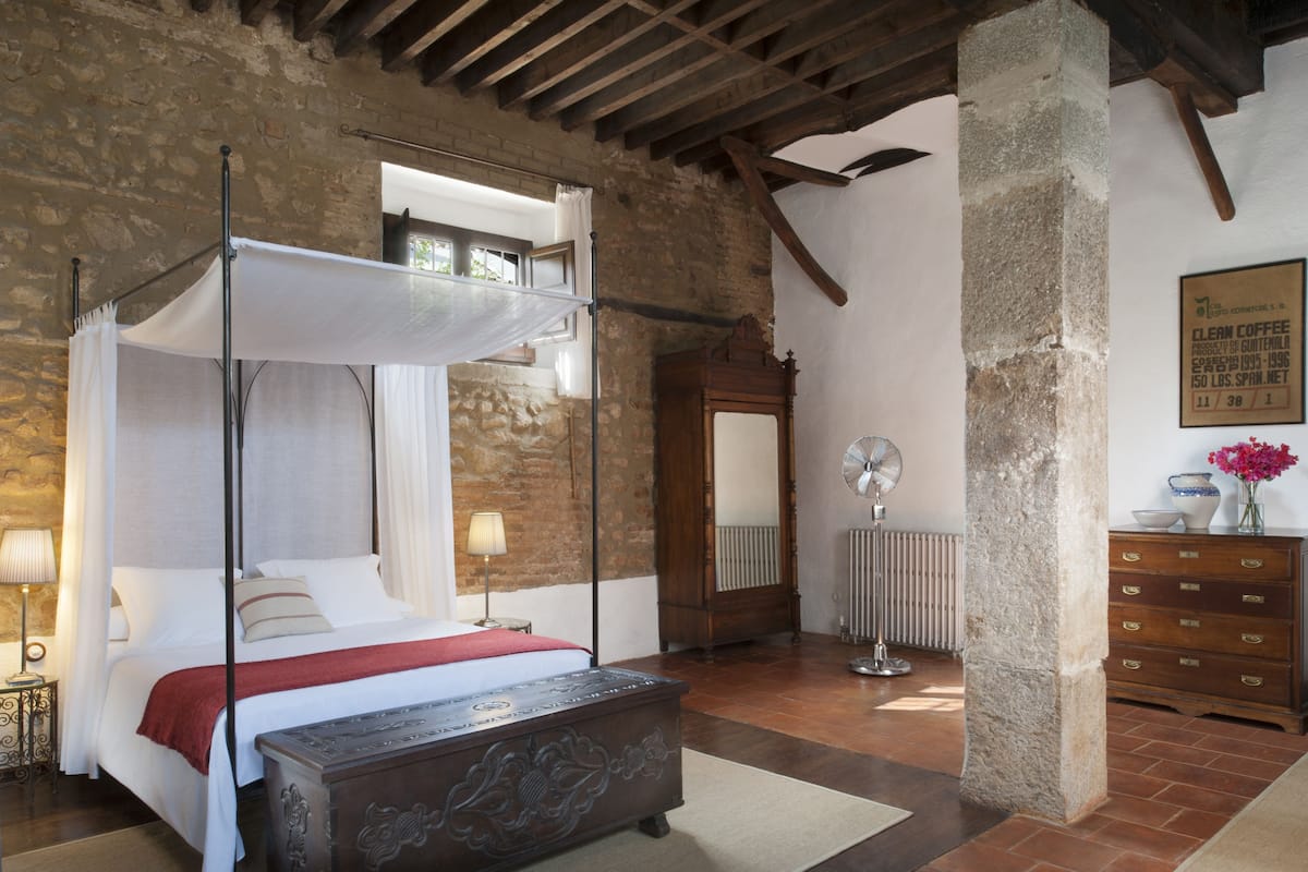 A bedroom with a four-poster bed, a wooden bench, a radiator, and a dresser.