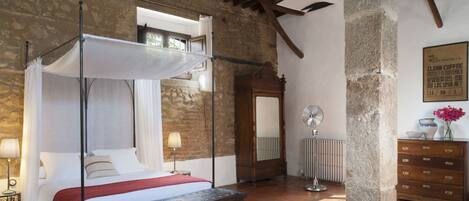 Un dormitorio con cama con dosel, un banco de madera, un radiador y un aparador.