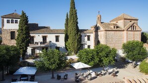 Un patio con mesas al aire libre, un edificio de piedra con un campanario y un árbol grande.