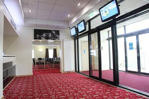 Un vestíbulo de hotel con alfombra roja, puertas de vidrio y múltiples monitores en la pared.