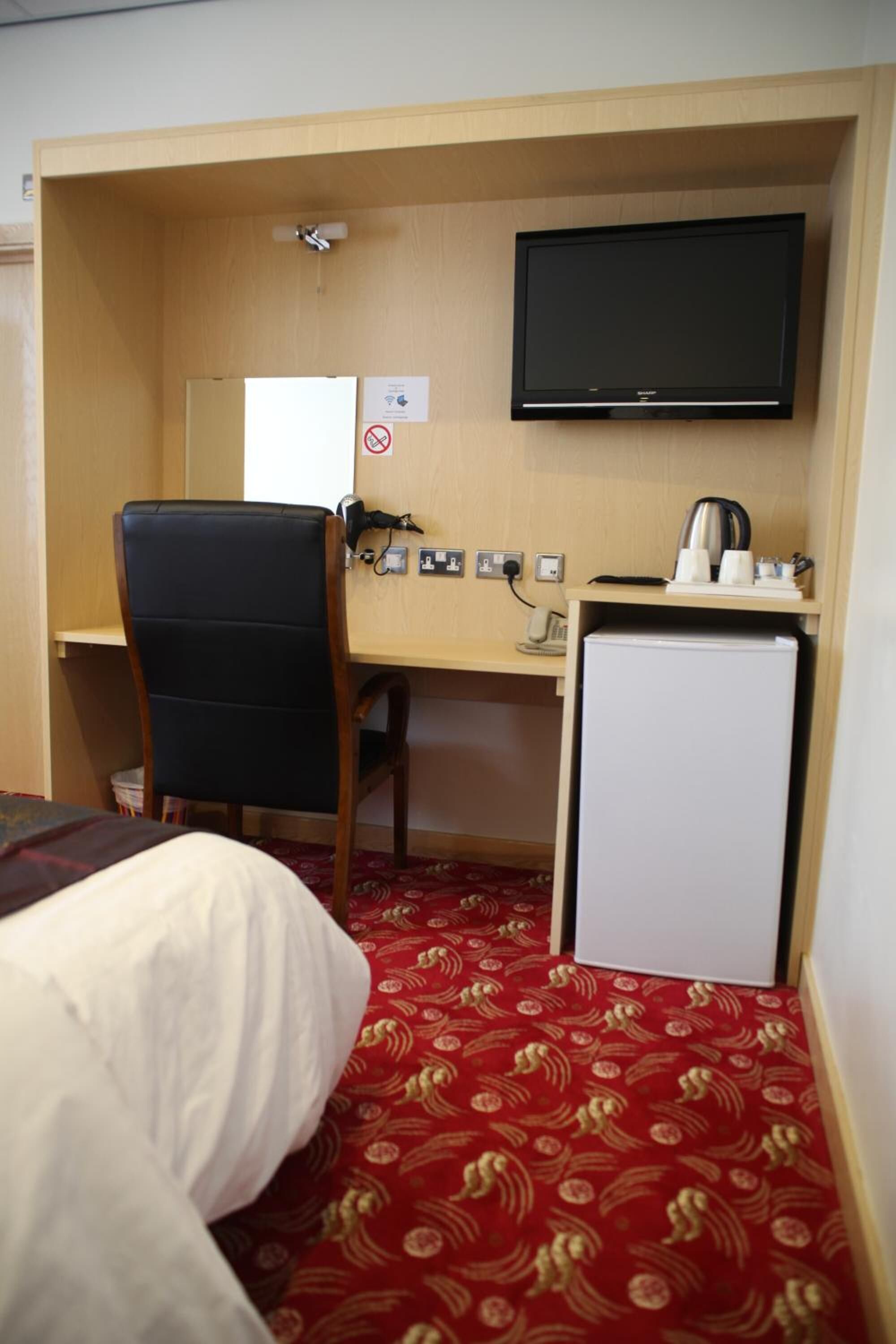 A hotel room with a bed, a desk, a chair, a television, and a small refrigerator.