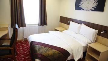 Quarto de hotel com cama, escrivaninha, cadeira e janela com cortinas.