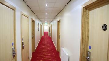 A hotel hallway with wooden doors, numbered room signs, and a red carpet.