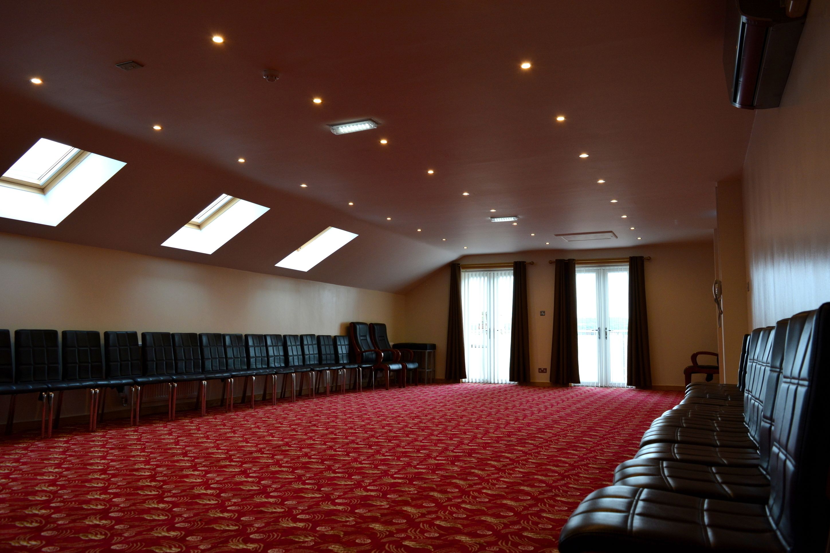 Un salón de conferencias con alfombra roja, filas de sillas, tragaluces y un ventanal grande.
