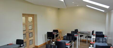 A conference room with tables and chairs, a wooden door, and a slanted ceiling with skylights.