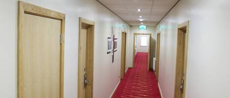 A hotel hallway with wooden doors, a red carpet, and white walls.