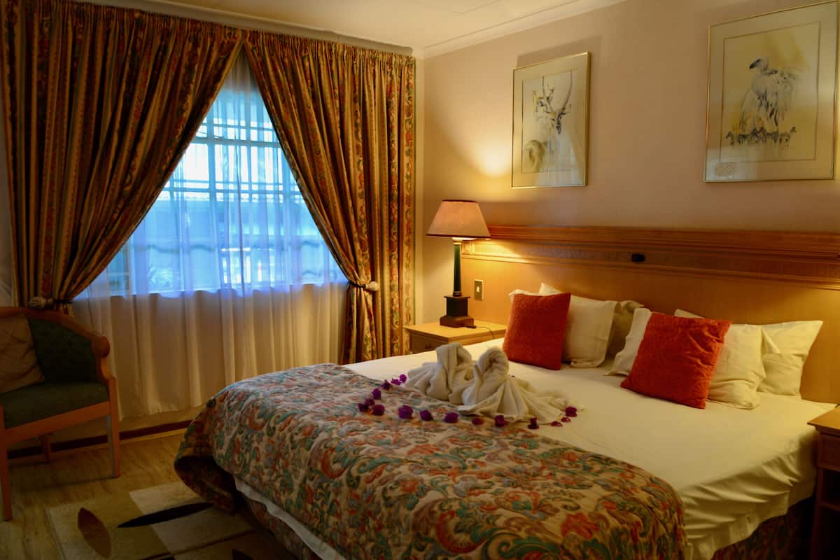 Una habitación de hotel con una cama, una silla, una mesita de noche con lámpara y cortinas.