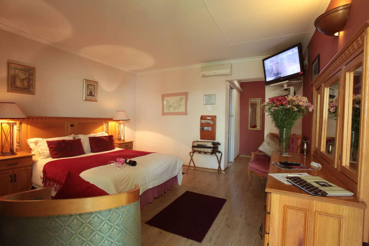 Habitación de hotel con una cama, lámparas de noche, televisor, escritorio con espejo y un jarrón con flores.