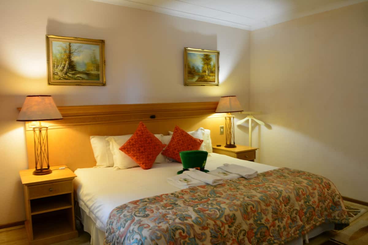 Habitación de hotel con cama, dos mesitas de noche, dos lámparas, dos cuadros en la pared y colcha estampada.