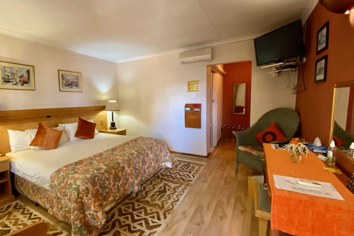 Habitación de hotel con cama, mesitas de noche, escritorio, silla, televisor y espejo.