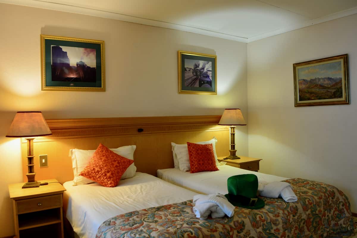 Habitación de hotel con dos camas, cada una con una colcha de diseño diferente, dos lámparas de noche y tres cuadros en las paredes.