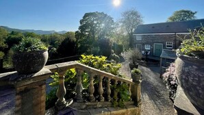 A view from a balcony overlooking a garden with potted plants and a building in the background. - Peterstone Court (Brecon)