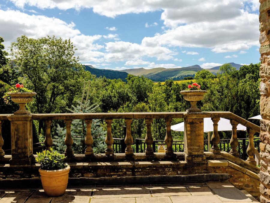 A stone balustrade with potted plants and a view of a mountainous landscape.