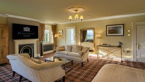 A living room with a fireplace, a sofa, a coffee table, and a television displaying 'Peterstone Court'. - Peterstone Court (Brecon)