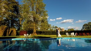 A swimming pool with chairs and a bride and groom standing by the poolside. - Peterstone Court (Brecon)