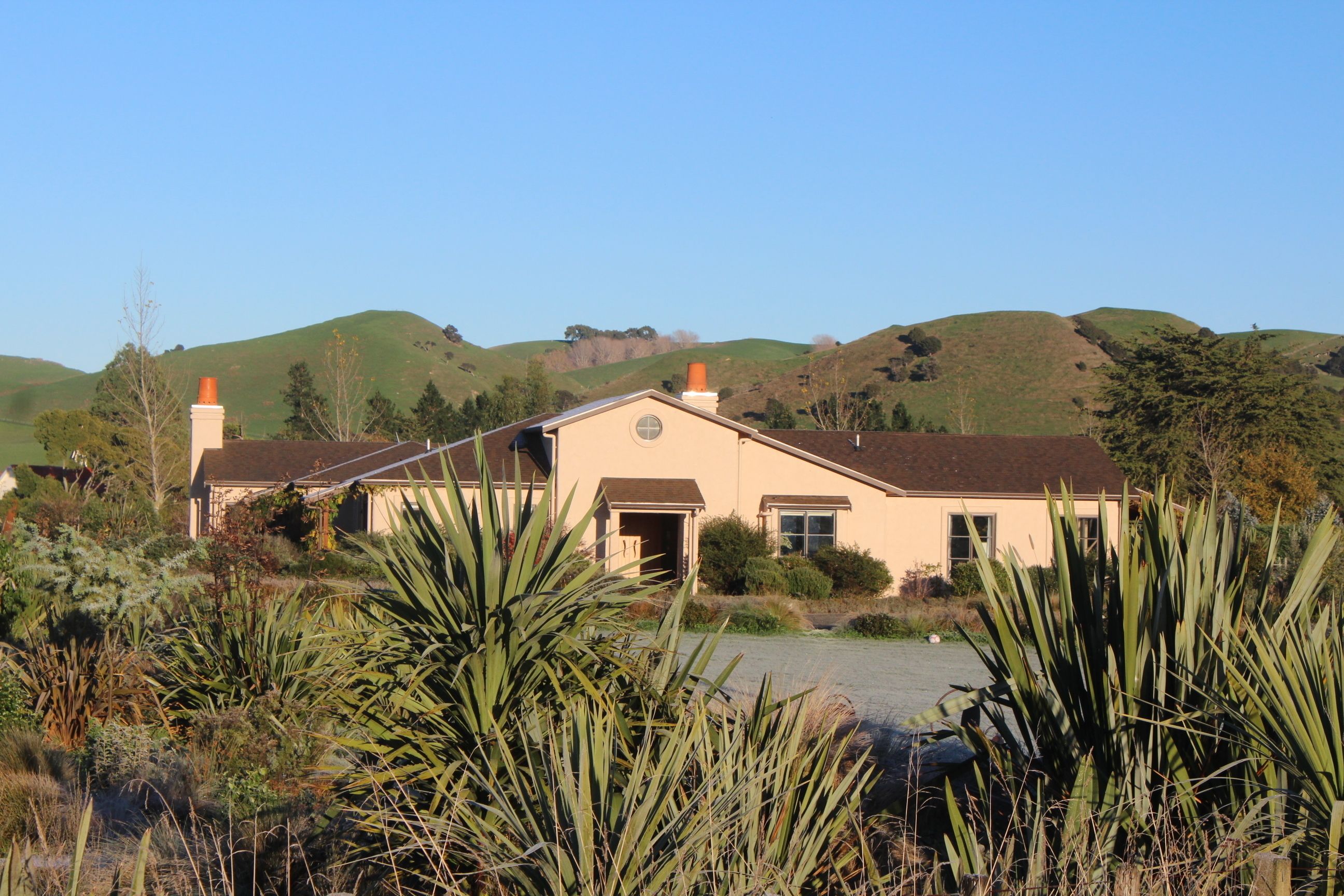 A two-story house with a front porch, surrounded by lush greenery and hills in the background.
