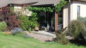 A house with a covered patio, a garden with various plants, and a dog resting on the patio. - The Summit Lodge (Gladstone)