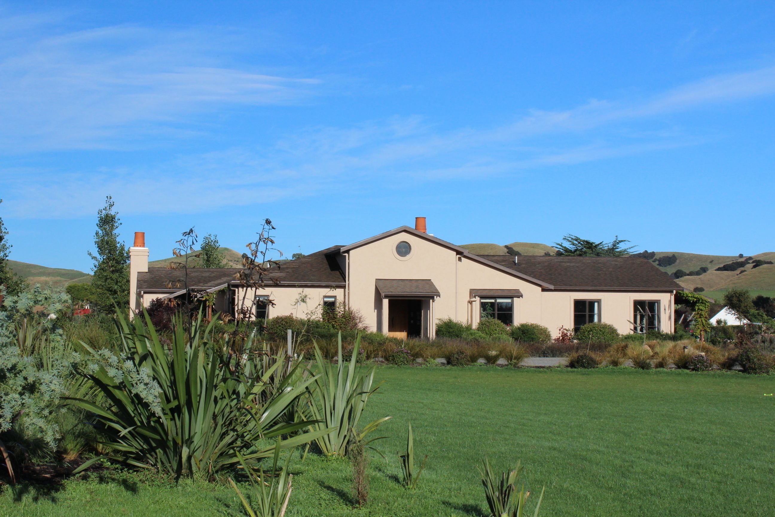 A two-story house with a large front lawn and a hilly landscape in the background.
