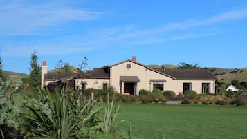 A two-story house with a large front lawn and a hilly landscape in the background.