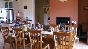 A dining area with wooden chairs and a table set for a meal, a kitchen in the background, and a large wall clock. - The Summit Lodge (Gladstone)