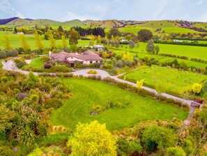 Una casa grande con un césped y jardín cuidados, rodeada de colinas onduladas y un cielo despejado.
