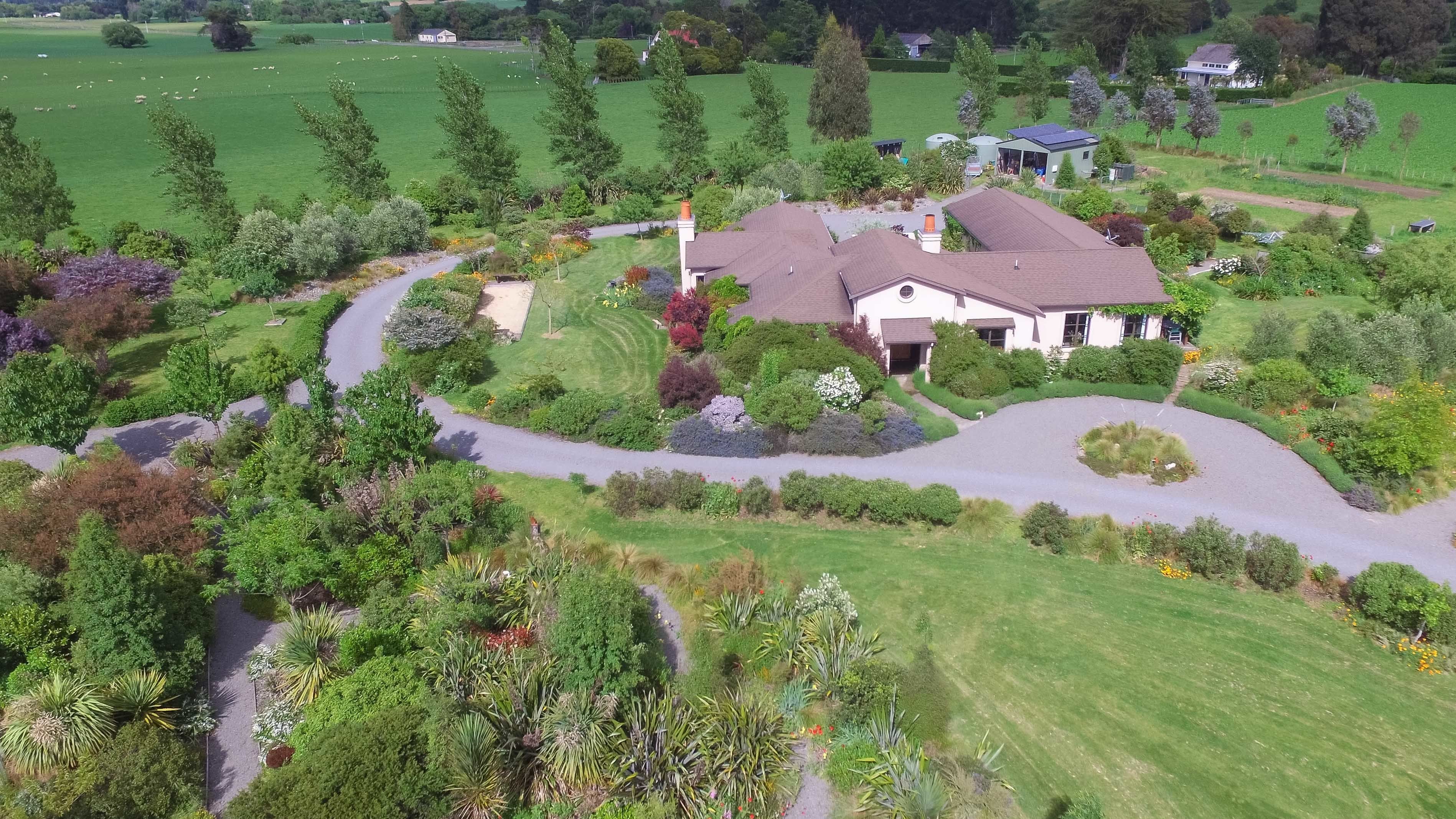An aerial view of a house surrounded by a well-maintained garden with a winding driveway.