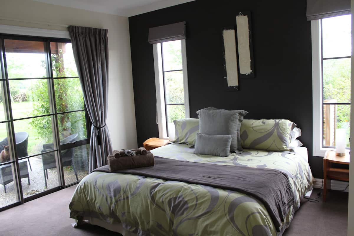 Quarto com uma cama grande, janela com cortinas e vista para o verde lá fora.