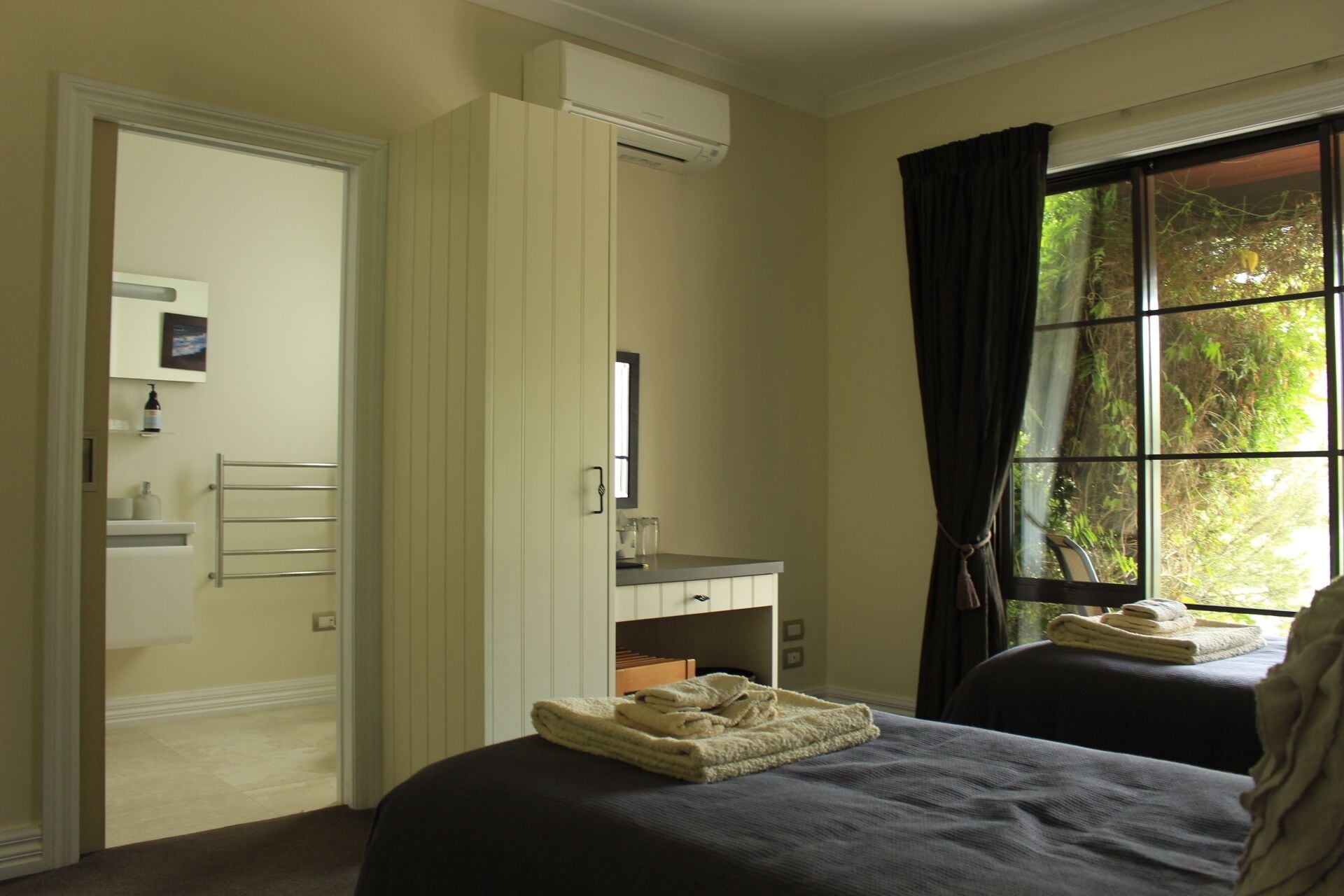 Un dormitorio con dos camas, un armario, un baño y una ventana con cortinas.