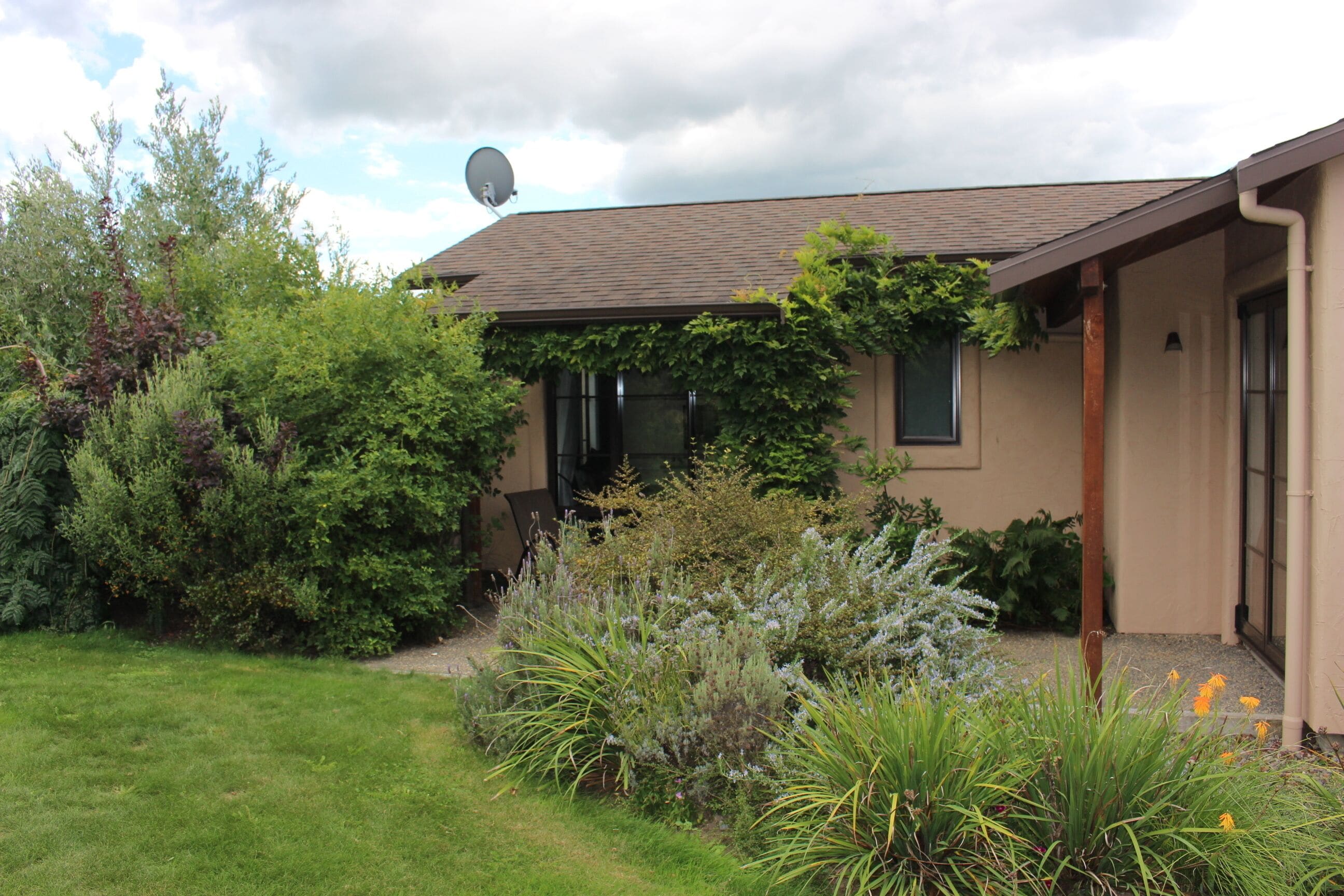 Ein Haus mit Satellitenschüssel, umgeben von einem Garten mit verschiedenen Pflanzen und Blumen.