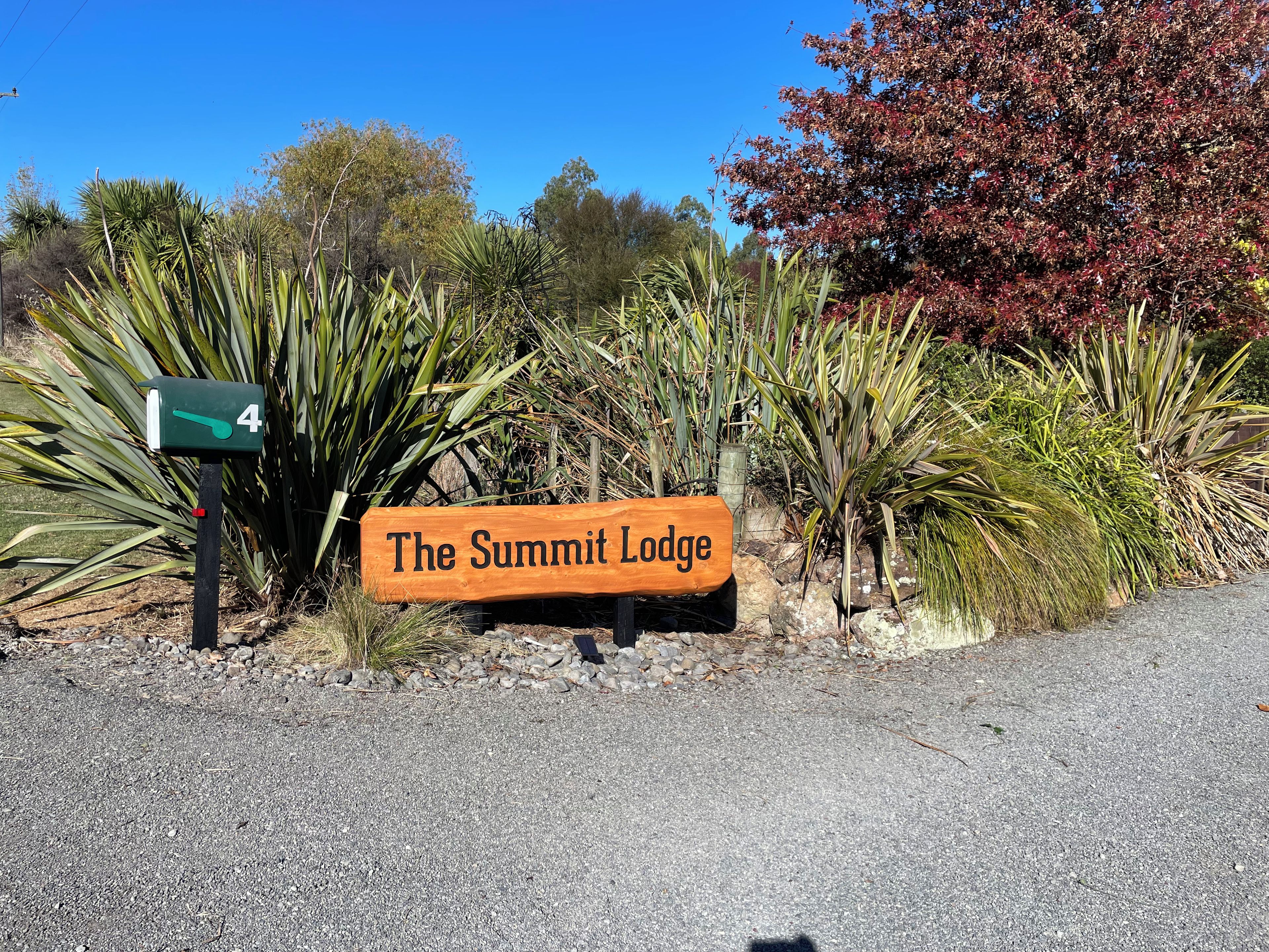 Señal de 'The Summit Lodge' con un buzón con el número 4 y diversas plantas al fondo.