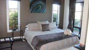 A bedroom with a bed, two windows, a painting, and a small table with towels. - The Summit Lodge (Gladstone)