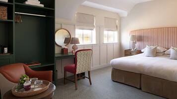 A hotel room with a bed, a desk with a chair, a round mirror, and a small table with a tray.