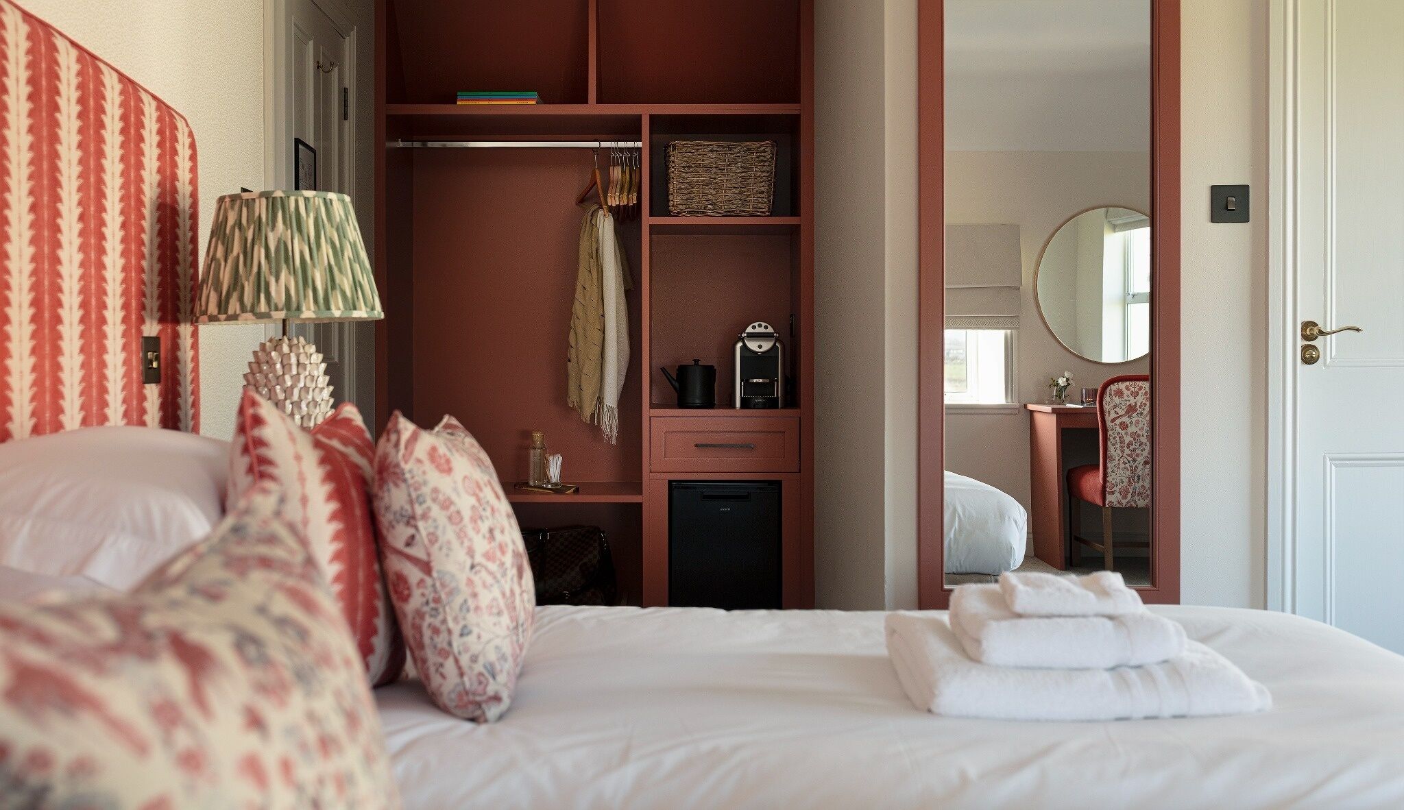 A bedroom with a bed, a bedside table, a mirror, a wardrobe, and a desk with a chair.