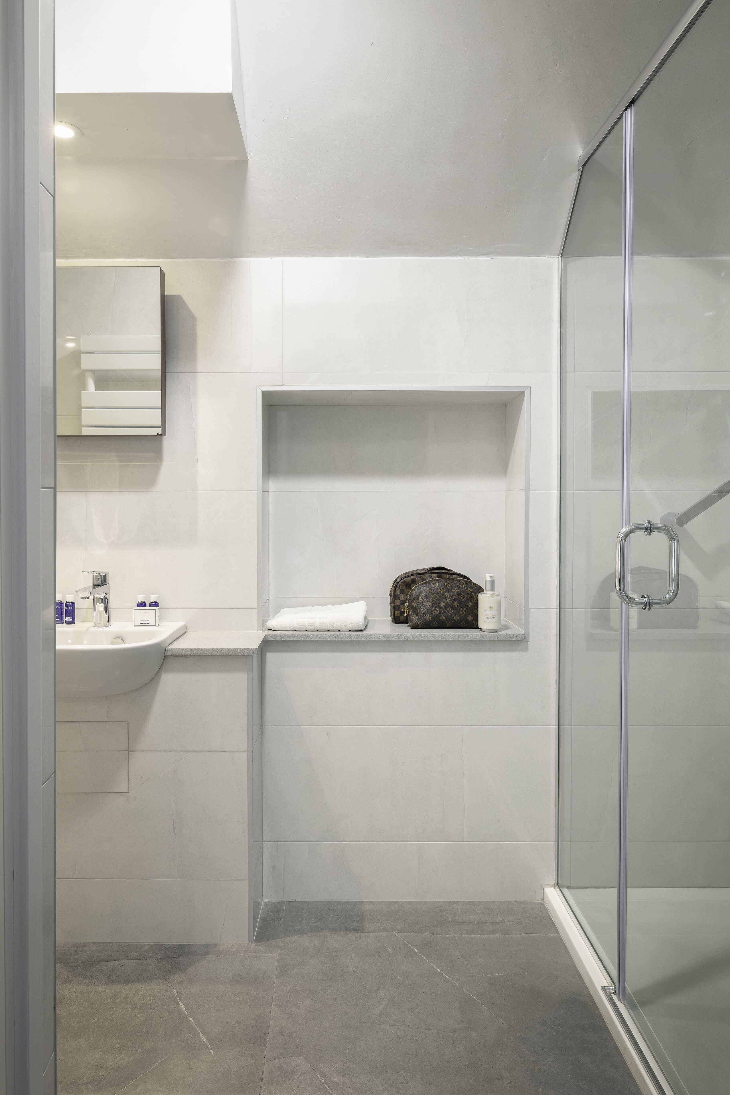 Une salle de bain moderne avec une douche à parois de verre, un meuble-lavabo avec un miroir et une étagère pour les articles de toilette.