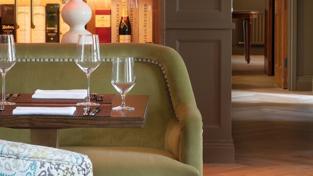 A green sofa with a table set for two, a wine rack in the background, and a lamp. - Teach de Broc (Ballybunion)