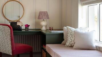 A bedroom with a green dresser, a red chair, a bed with striped bedding, a round mirror, and a lamp.