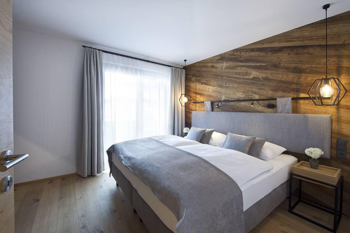 Une chambre moderne avec un grand lit, un lambris en bois, une table de chevet avec une lampe et une fenêtre avec des rideaux.