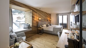 Habitación de hotel moderna con una pared decorada en madera, una cama grande, un área de estar con vistas y una mesa de comedor con alimentos para el desayuno.