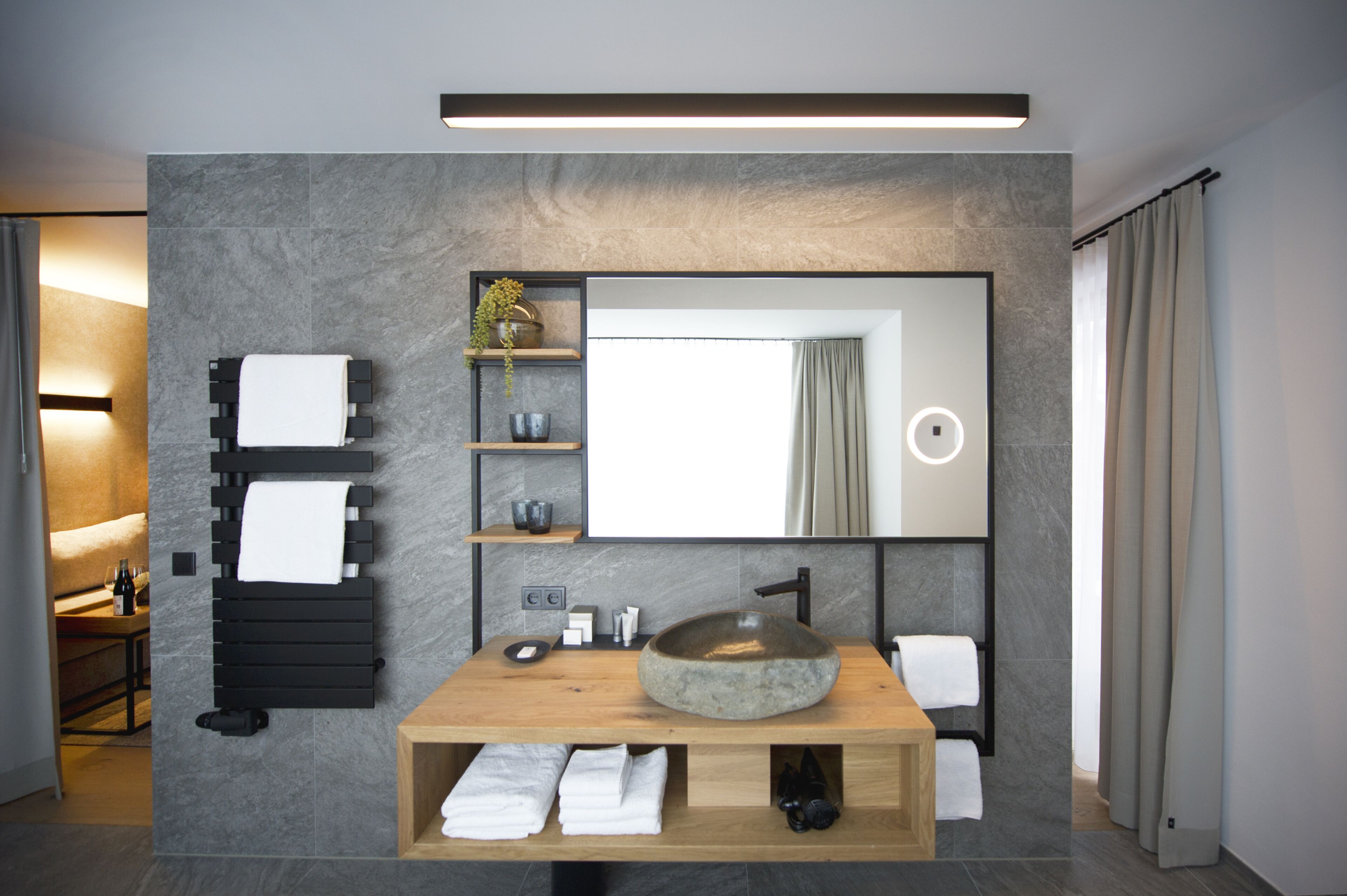 A modern bathroom with a large mirror, a wooden vanity, and a stone sink.