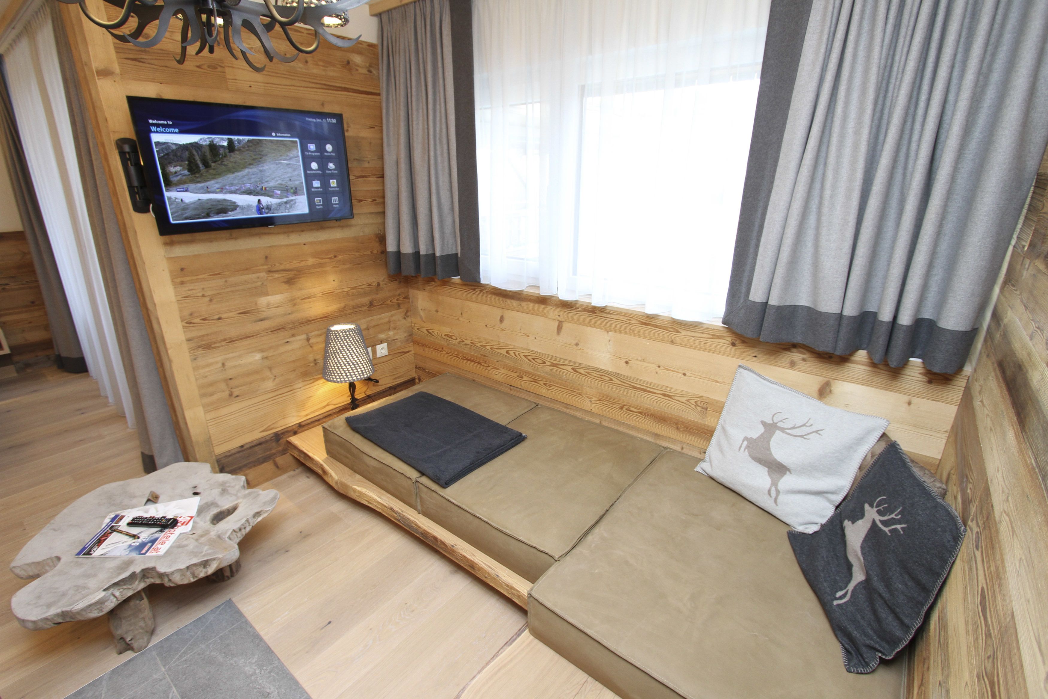Una habitación acogedora con detalles de madera, un televisor de pared, un sofá con cojines y una ventana con cortinas.