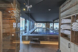 Un área de spa moderna con un hidromasaje envuelto en cristal, estanterías de madera con toallas y vistas a la ciudad.