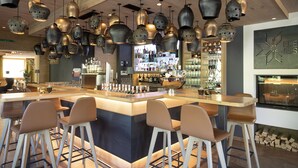 Zona de bar con una isla central, varias lámparas colgantes y una variedad de utensilios y botellas.