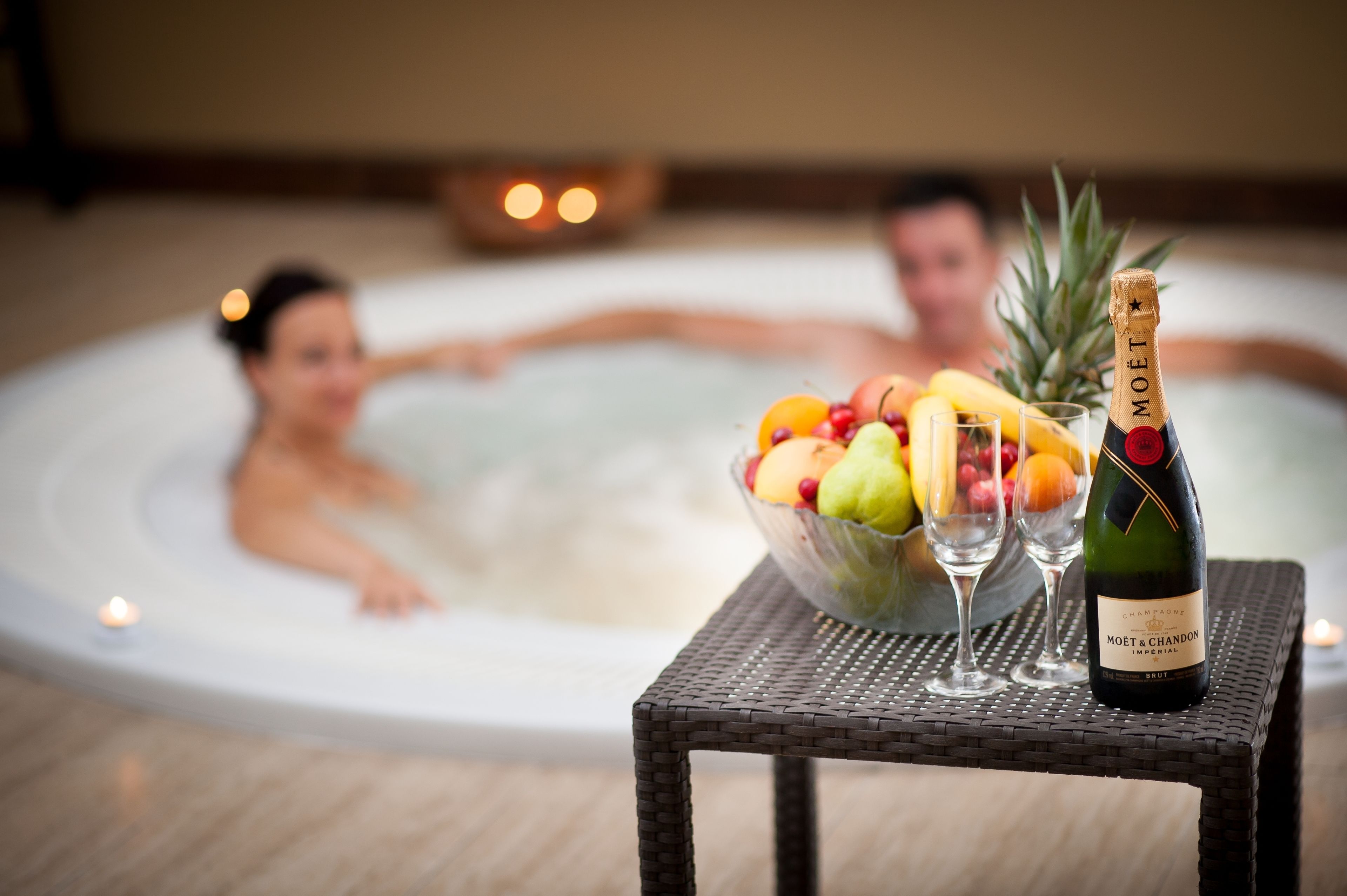 A hot tub with a table in the foreground holding a bottle of Moët champagne, a bowl of fruit, and two glasses.