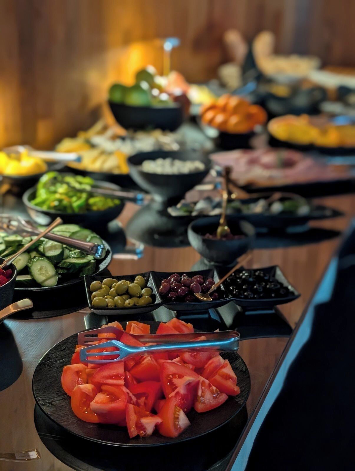 Een buffet met verschillende soorten eten, zoals plakjes komkommer, olijven, tomaten en andere groenten.