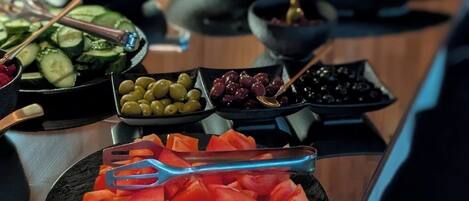 Een buffet met verschillende soorten eten, zoals plakjes komkommer, olijven, tomaten en andere groenten.