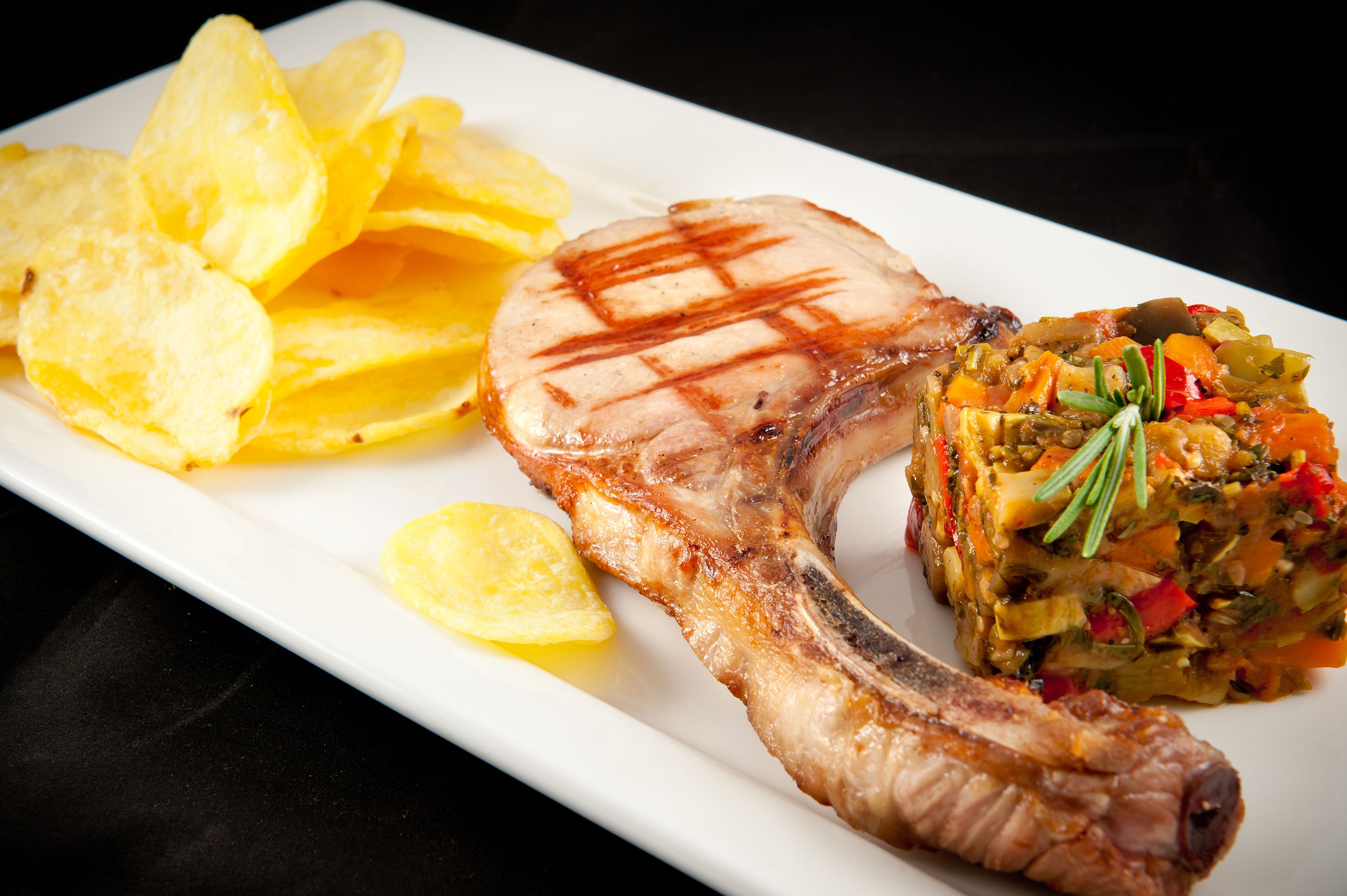 A plate with a grilled steak, a vegetable medley, and potato chips.
