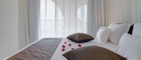 A neatly made bed with white and brown bedding, a window with sheer curtains, and a view of the outside.