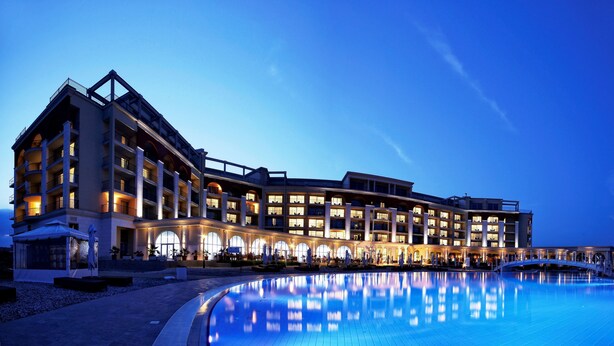 Un hotel de varios pisos con piscina, mobiliario exterior y un paseo techado.